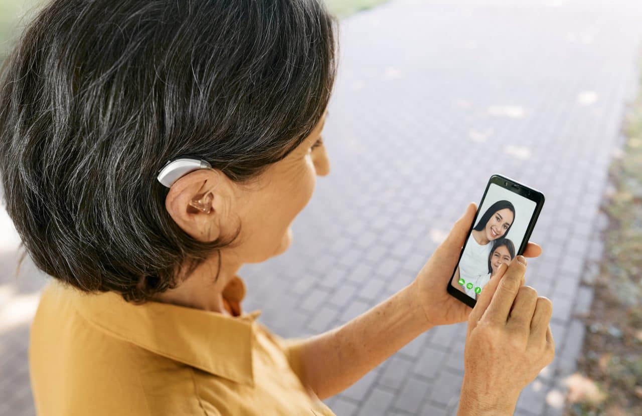 Woman with a hearing aid talks with her family during a video chat via her smartphone.