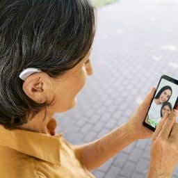 Woman with a hearing aid talks with her family during a video chat via her smartphone.