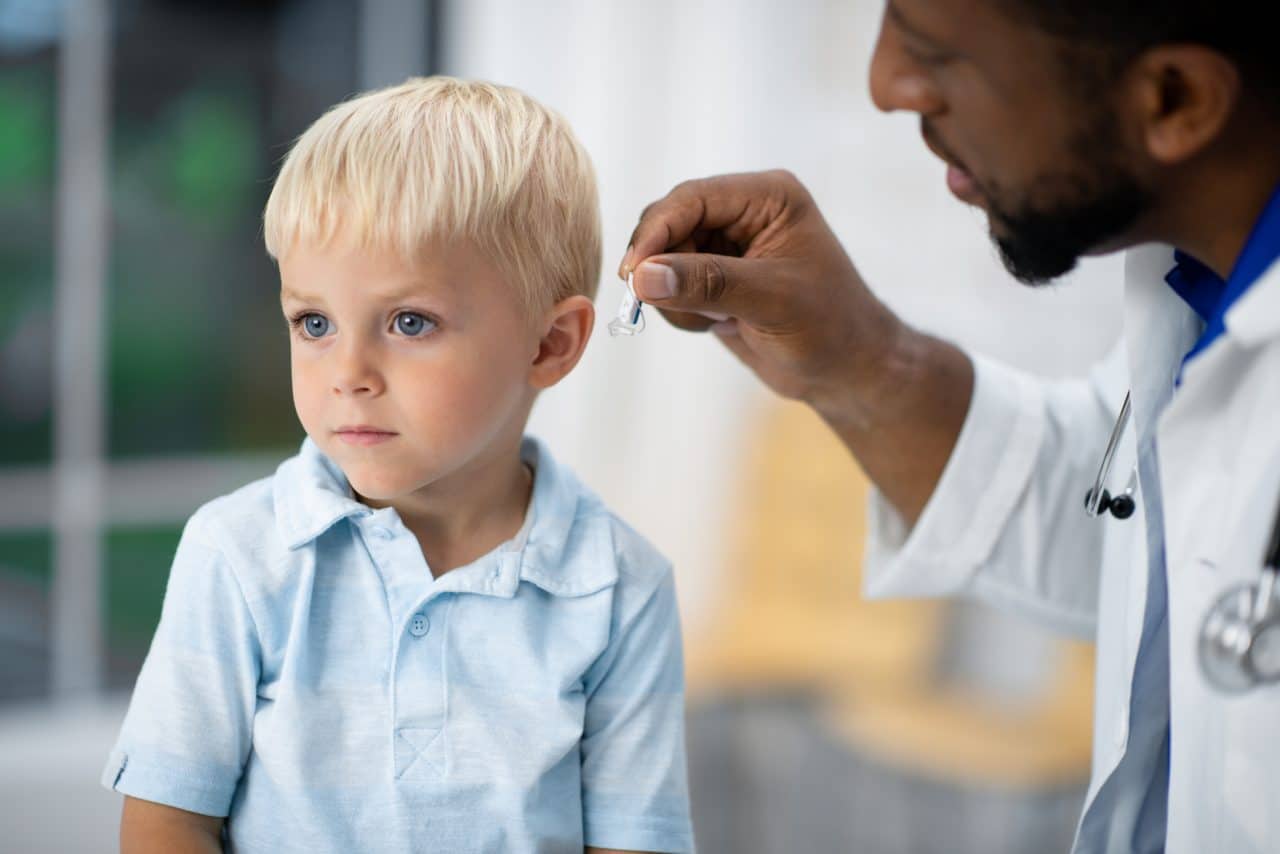 Audiologist fits little boy with a pediatric hearing aid.