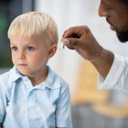 Audiologist fits little boy with a pediatric hearing aid.