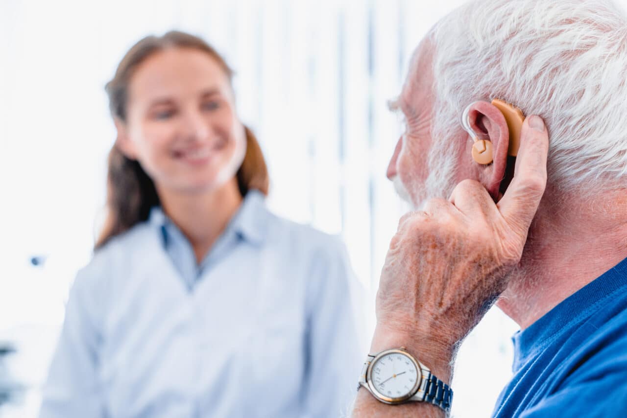 Older patient wearing a hearing aid while talking to his audiologist.
