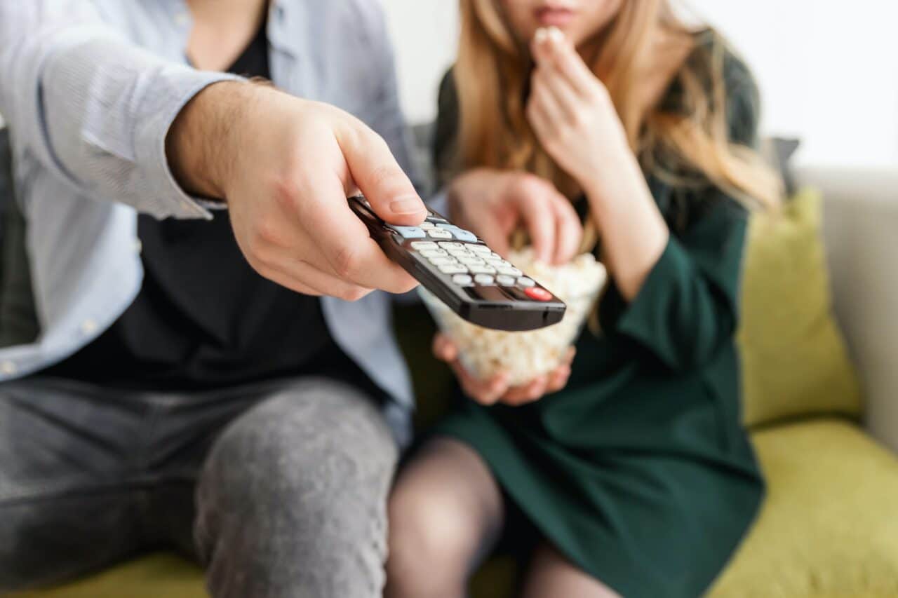 Close-up of a TV remote with couple watching TV.