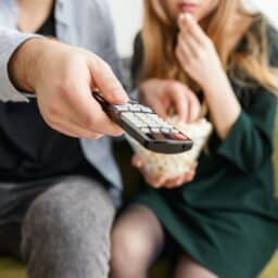 Close-up of a TV remote with couple watching TV.