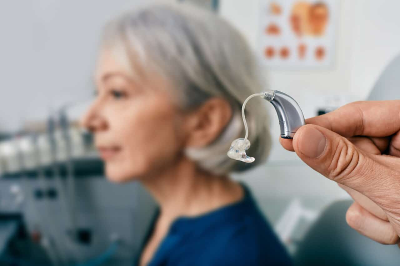 Close-up of hearing aid near senior patient's ear at audiology clinic. Hearing solutions, hearing BTE aids