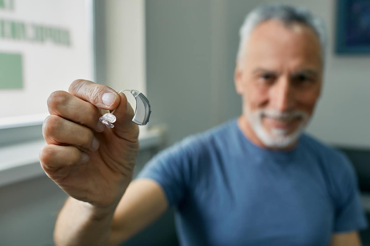 Senior man holding up a hearing aid.