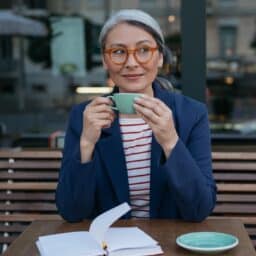 woman sitting at cafe outdoors with red glasses, holding warm tea